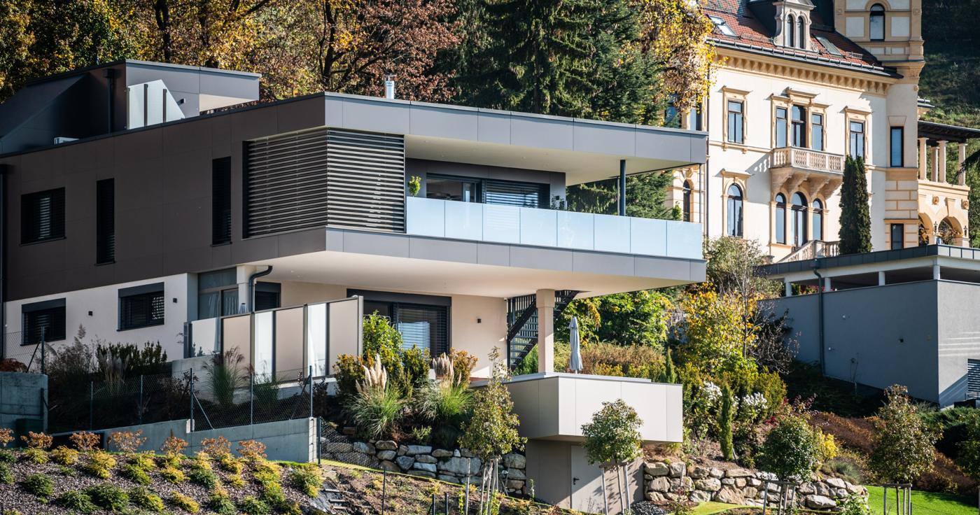 Wohnhaus mit auskragender Terrasse und Lamellen neben historischer Villa im Herbst
